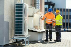 Two Electricians Men Wearing Safety Jackets Checking Air Conditioning Unit On Building Rooftop
