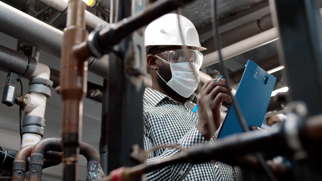 African mechanical supervisor in safety mask doing inspection on plant.